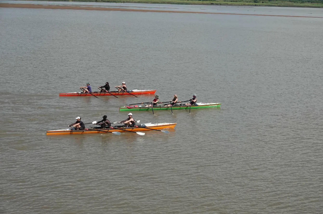 Three RowZambezi triple sculls rowing in formation on a wide, calm river