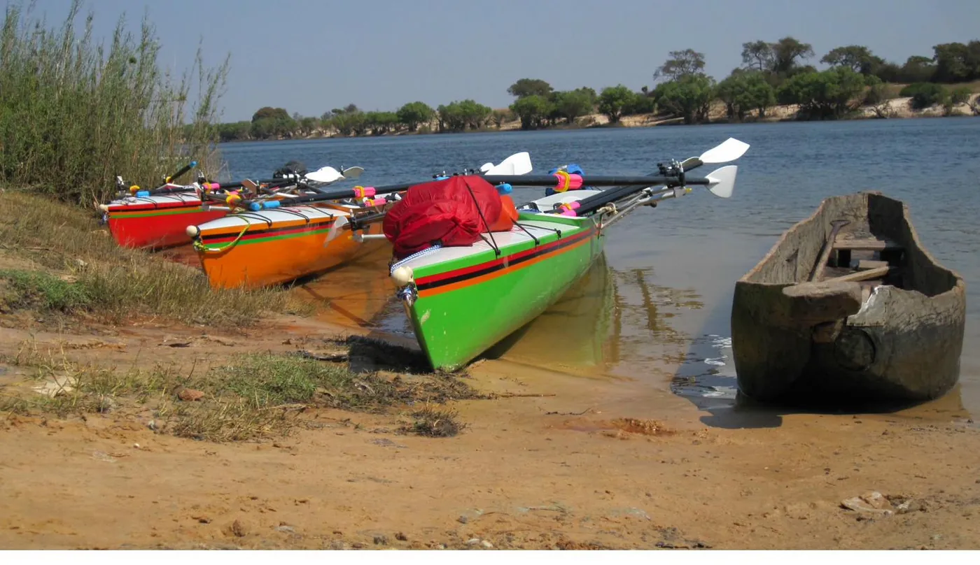 RowZambezi triple sculls pulled up on the riverbank beside a dugout canoe